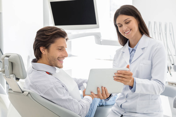 cheerful dentist showing patient results of treatment on digital tablet